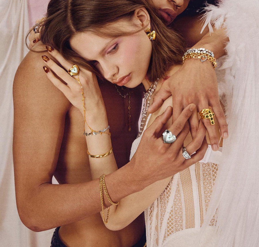 Romantic close-up of a couple wearing mixed metal jewelry, featuring unique heart watch rings and layered gold bracelets.