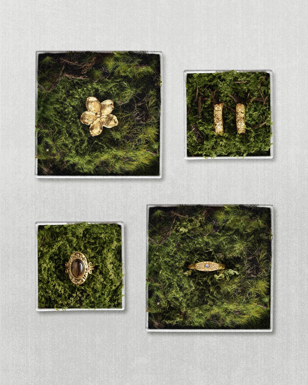 Four beautifully crafted gold jewelry pieces, including textured rings, hoop earrings, and a flower design, displayed elegantly on square beds of green moss highlighting nature-inspired aesthetics.