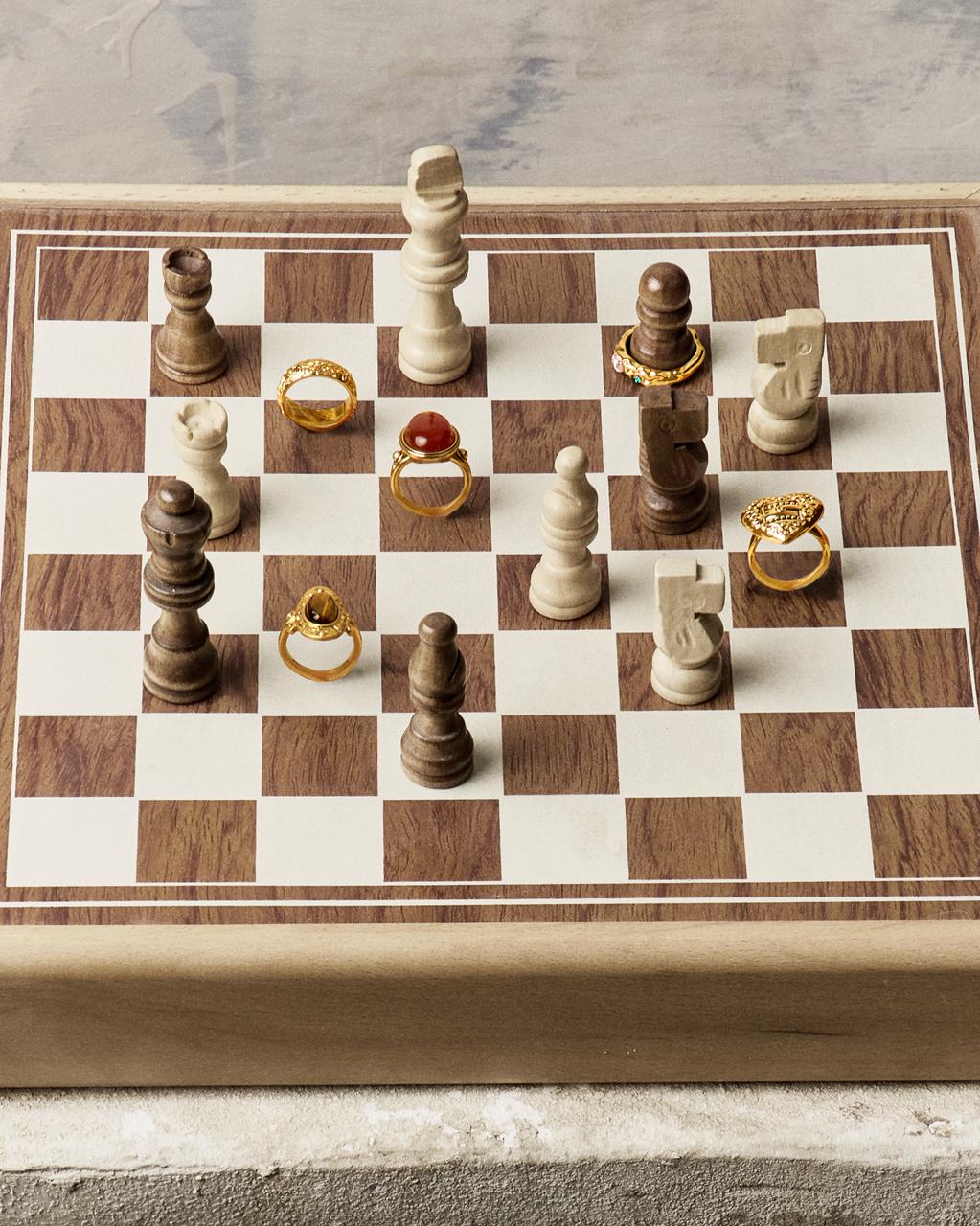 A wooden chessboard featuring various en route gold rings, including a unique heart design and carnelian stone.