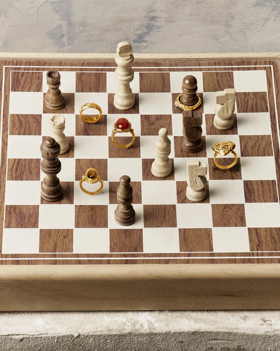 A wooden chessboard featuring various en route gold rings, including a unique heart design and carnelian stone.
