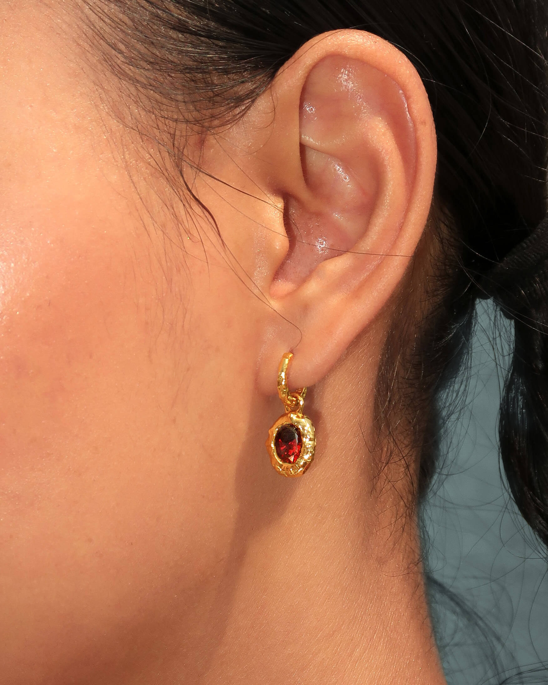 Modelo usando pendientes dorados de piedra de nacimiento con un diseño de gema granate de inspiración vintage.